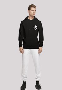 Svart hoodie med framficka, dragsko och en vit globlogotyp på vänster bröst. Kombineras med vita joggers och svarta sneakers.