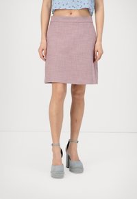 Falda rosa texturizada en línea A con cintura ajustada y dobladillo que cae por encima de la rodilla, combinada con zapatos de plataforma grises con correas al tobillo.