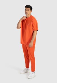 Oranžové tričko s krátkým rukávem a odpovídající zúžené kalhoty vyrobené z měkkého materiálu, doplněné o bílé tenisky. Minimalistický design a volný střih.