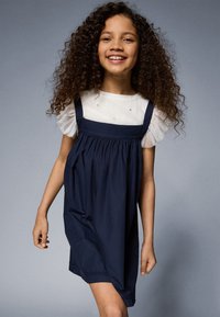 Mørkeblå kjole med løs passform, har justerbare stropper, en rynket bodice og en hvit skjorte med pufferm og gull detaljer.