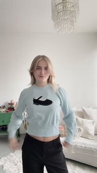 Suéter azul claro cropped com textura canelada e mangas bufantes, com um desenho de sapato preto na frente. Combinado com calças pretas.