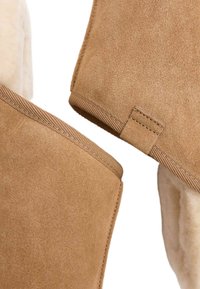 Tan ruskinds slippers med en blød cremet foring, der har en robust brun sål og en struktureret sidetop med stikninger.
