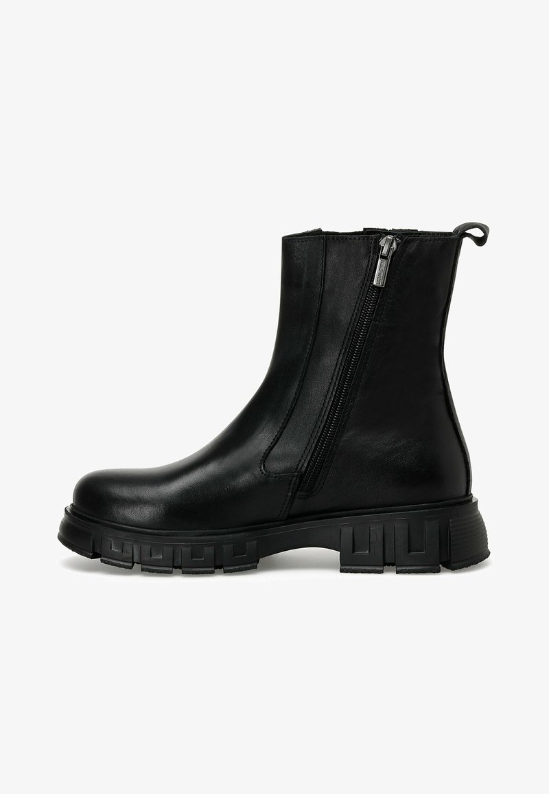 Bottine noire en cuir avec semelle épaisse à relief, fermeture éclair latérale et languette à l'arrière, montrée de côté extérieur sur fond blanc.