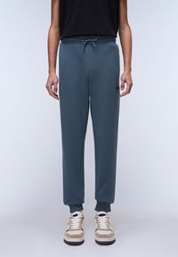 Dark blue sweatpants with an elastic waistband and drawstring, featuring side pockets and ribbed cuffs. Paired with beige and white sneakers.