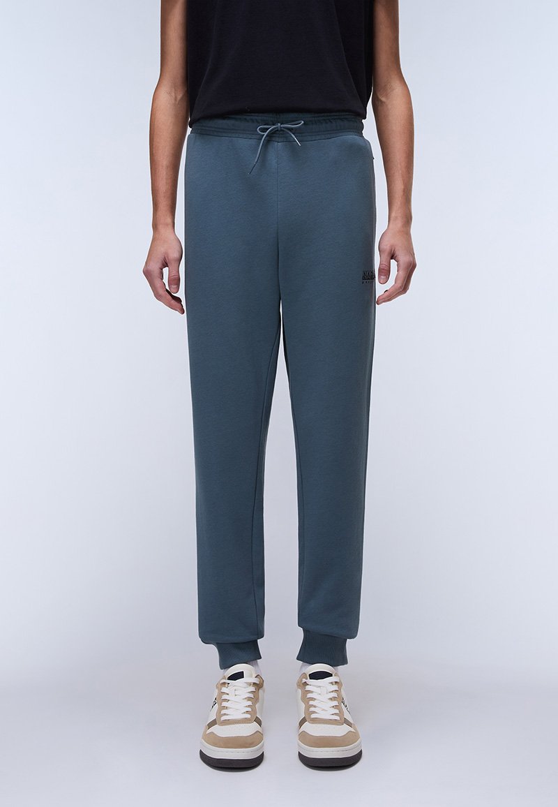Dark blue sweatpants with an elastic waistband and drawstring, featuring side pockets and ribbed cuffs. Paired with beige and white sneakers.