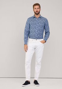 Camisa de manga larga azul con un estampado y jeans blancos con zapatillas negras. La camisa presenta un diseño floral; los jeans son ajustados y de color blanco sólido.