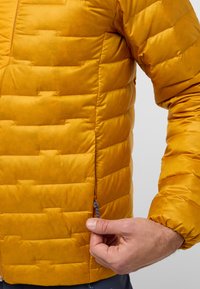Giacca a vento gialla con design trapuntato e dettagli con zipper laterale. Il materiale sembra liscio e leggero. Presenta polsini elasticizzati.