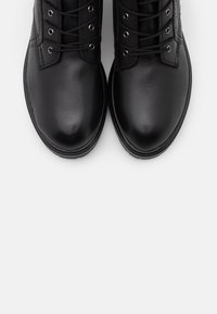 Zapatos de cuero negros con puntas redondeadas, cordones planos y ojetes de metal. Textura suave con un sutil detalle de costura, sobre un fondo blanco.