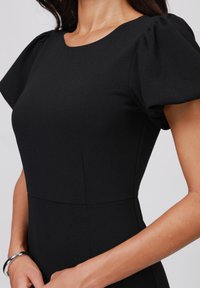 Robe noire avec des manches bouffantes courtes, un col rond et une silhouette ajustée avec des détails de couture. Texture lisse et coupe élégante.