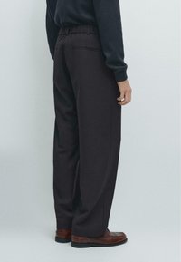 Černé široké kalhoty s elastickým pasem, vybavené bočními kapsami a hladkou texturou, doplněné hnědými koženými botami.