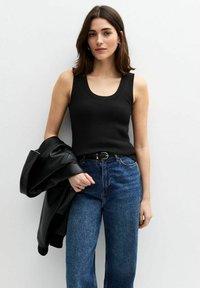 Svart ribbad linne med rundad halsringning, kombinerat med högmidjade blå denimjeans. En svart läderjacka hängande över ena armen.