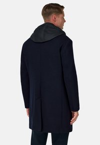 Tmavě modrý kabát z vlněné směsi s černou kapucí, s jedním zadním rozparkem a bočními kapsami, hladkým povrchem a střihaným designem.