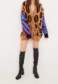 Brun kofta med leopardmönster och blå- och rödrandiga ärmar, med v-ringning, knappstängning och kontrasterande svarta muddar.