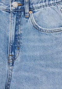 Jean en denim bleu clair avec surpiqûres contrastantes, fermeture par bouton métal et une poche avant unique aux bords effilochés.