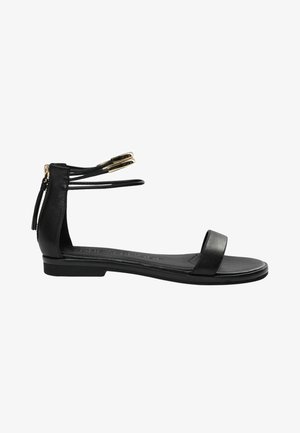 Zwart platte sandaal met ritssluiting bij de enkel, open teen en twee dunne enkelbandjes met gouden uiteinden.