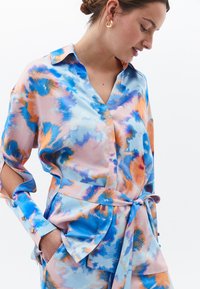 Zijde blouse met een lichte, vloeiende vormgeving. Kleurrijke mix van blauwe, oranje en roze patronen. Inclusief een strik in de taille en manchetmouwen.