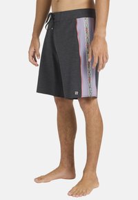 Σκούρα γκρι μαγιό βερμούδα με χαλαρή εφαρμογή, διακοσμημένο με πολύχρωμο λουλουδάτο μοτίβο στο πλάι και αντίθετη ροζ διακόσμηση.