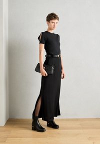Abito nero a costine con maniche corte, aperture laterali, cinched con una cintura nera. Abbinato a stivali neri con tacco e una pochette nera.