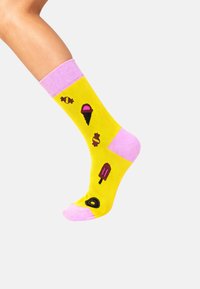 Gule bomuldssokker med lyserøde manchetter, der har broderede motiver af is, slik og en ispind i kontrasterende farver.