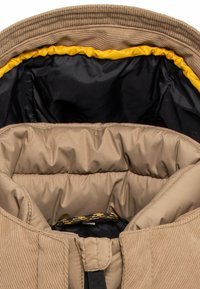 Beige Daunenjacke mit Rippenkragen, schwarz-gelbem Innenfutter. Sie verfügt über eine gesteppten Innentextur, glatten Außenstoff und einen Reißverschluss.