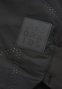 Svart tyg med en jämn textur som har en upphöjd rektangulär etikett präglingen med "COLOR KIDS" och små perforeringar runt den.