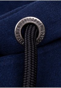Tessuto blu navy con un motivo testurizzato presenta un occhiello metallico con inciso "SPITZBUB", che tiene un cordoncino nero intrecciato.