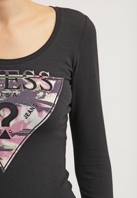 Maglietta nera a maniche lunghe con un design grafico che presenta un emblema triangolare e del testo, realizzata in un morbido tessuto misto cotone.