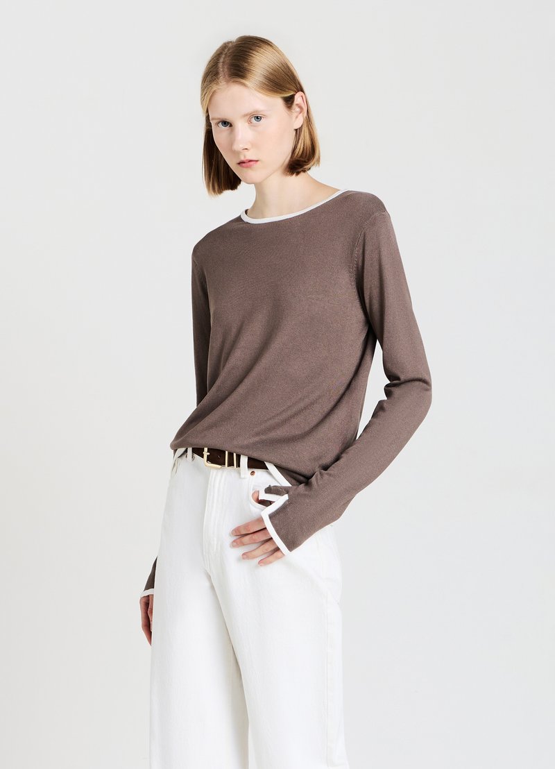 Maglietta marrone a maniche lunghe con scollatura bianca, caratterizzata da polsini allungati. Abbinata a pantaloni bianchi a vita alta, che mettono in risalto una vestibilità rilassata.