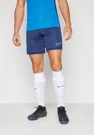 Nike sportsudstyr bestående af en blå skjorte og marineblå shorts. Sorte støvler med blå detaljer. Hvide sokker med blå Nike-logo og mønstret tekstur.