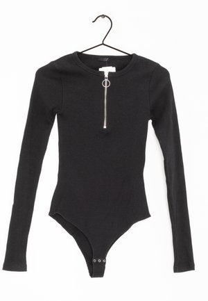 Zwart ribgebreid bodysuit met lange mouwen, zilveren rits aan de voorkant en drukknoopsluiting bij het kruis, hangend aan een zwarte hanger tegen een witte achtergrond.