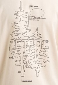Beiger Stoff mit schwarzen Linienzeichnungen von immergrünen Bäumen und dem Text "PETROL" in fetter Schrift. Enthält Referenz- und Unternehmensdaten.