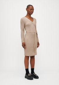 Beige ribbet strikket omslagskjole med lange ermer, tettsittende midje og knyting. Båret med svarte plattform loafers og ribbete sokker.