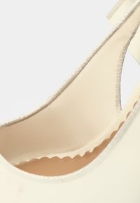 Intérieur de chaussure beige avec une surface lisse, doté d'un bord festonné le long de la doublure et d'un subtil liseré métallique. Design minimaliste.