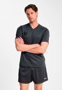 Atletyczna ciemnoszara sportowa koszulka z dekoltem w serek, krótkimi rękawami i fakturowanym wykończeniem. Noszona z dopasowanymi czarnymi sportowymi szortami.