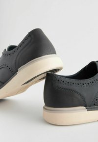 Zapatos de cuero gris oscuro con detalles perforados, suelas de goma gris claro y costuras en contraste, con un diseño de bajo perfil.