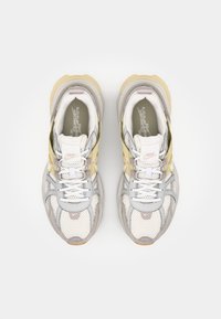 Baskets Nike avec une tige en mesh gris et blanc cassé, rehaussées d'empiècements jaunes et gris clair, dotées de lacets blancs et d'une semelle texturée.