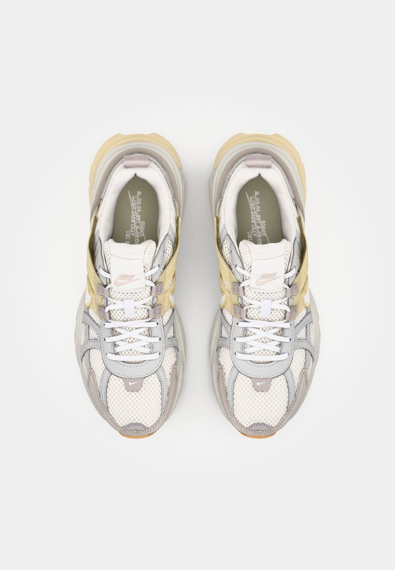 Nike-Sneaker mit einem grauen und cremefarbenen Mesh-Obermaterial, akzentuiert durch gelbe und hellgraue Überzüge, mit weißen Schnürsenkeln und einer strukturierten Sohle.