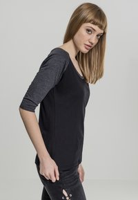 Svart langermet skjorte med grå ermer, rund hals og en tettsittende design. Glatt tekstur med minimale detaljer. Passer for uformell bruk.