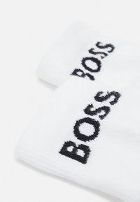 Vita bomullssockor med svart broderad varumärkesnamn "BOSS" i fet stil. Texturerad tyg med ribbad ankel-design.