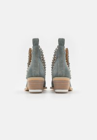 Botas de tobillo de ante verde con un bajo tacón apilado, adornos de tachuelas a lo largo de los lados y un forro interno de color marrón claro en contraste.