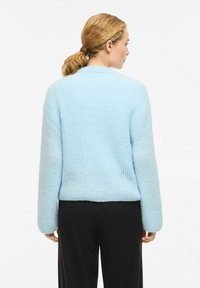 Helehall sinine soonikkoes kampsun, millel on pikad varrukad ja ümmargune kaelus, tekstuurse viimistlusega ja lõdva lõikega, sobitatuna mustade pükstega.