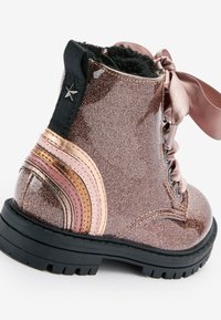 Dziecięce błyszczące różowe botki za kostkę z czarną podeszwą, satynowymi sznurowadłami, detalem w kształcie gwiazdy na czarnej pętelce i paskami metalicznych akcentów na obcasie.