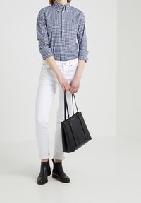 Marinblå och vit rutiga skjorta med knappar, vita tighta jeans, svarta chelsea boots och en svart tote-väska med guldaccenter.