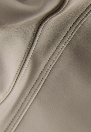 Hellbeiger Stoff mit glatter Textur und sichtbaren Nahtdetails, der eine diagonale Naht aufweist, die dem Design Tiefe verleiht.