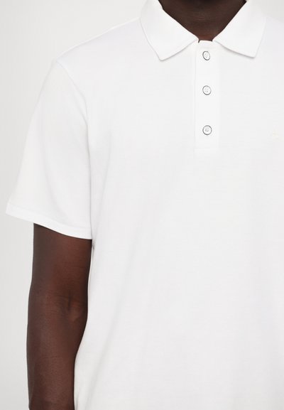 Chemise polo blanche en coton avec un col classique, patte de boutonnage à trois boutons, manches courtes et un petit logo.