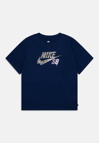 Navy zila kokvilnas t-krekls ar lielu, atstarotiem Nike logo un "SB" lavandas krāsā. Īsām piedurknēm un klasisku apaļu kakla izgriezumu.