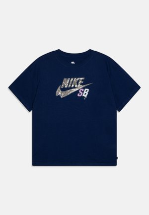 Námořnická modrá bavlněná tričko se velkým reflexním logem Nike a "SB" v levandulové barvě. Krátké rukávy a klasický kulatý výstřih.