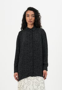 Schwarzes Langarmshirt mit blumigem Linienstreifenmuster, Button-Down-Kragen und abgerundetem Saum, kombiniert mit einem plissierten weißen Rock.