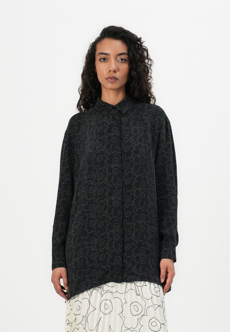 Schwarzes Langarmshirt mit blumigem Linienstreifenmuster, Button-Down-Kragen und abgerundetem Saum, kombiniert mit einem plissierten weißen Rock.