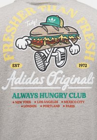 Dibujo animado de un sándwich con gorra verde y zapatillas, rodeado de texto que promociona Adidas Originals y nombres de ciudades.